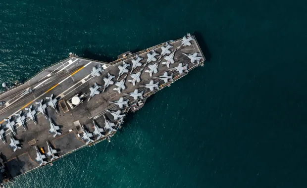 Aerial view of an aircraft carrier with multiple fighter jets lined up on the front