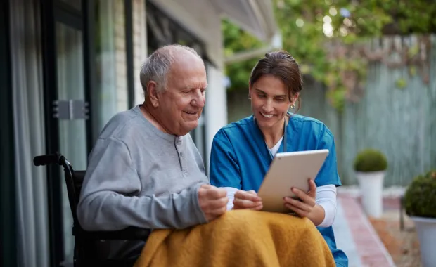 Care worker sitting with elderly patient looking at Ipad 