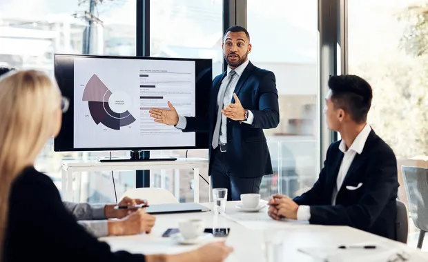 A business man presenting to two colleagues on a large monitor