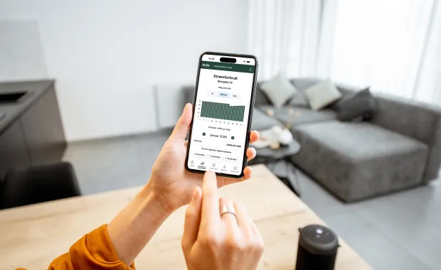 Person holder mobil med app for strømforbruk i hjemmemiljø.