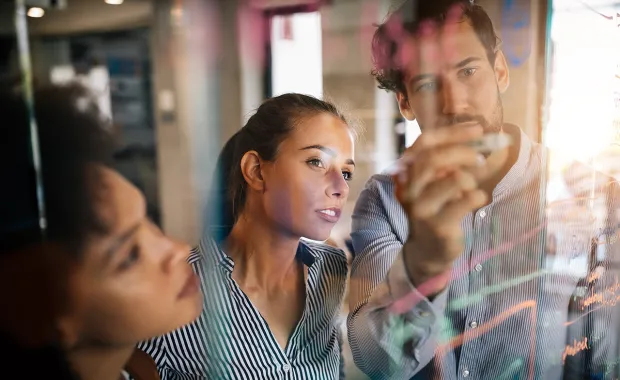 three people looking at a whiteboard