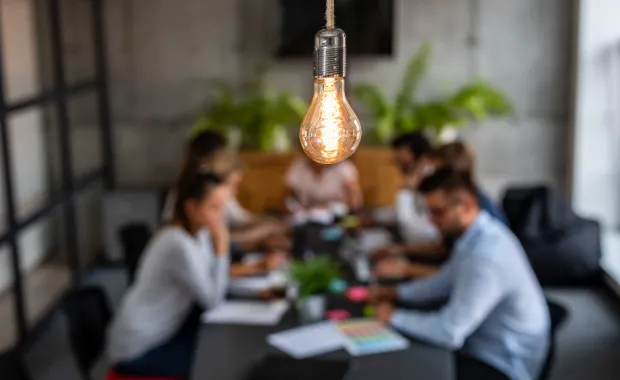team of people sitting around conference table under glowing light bulb