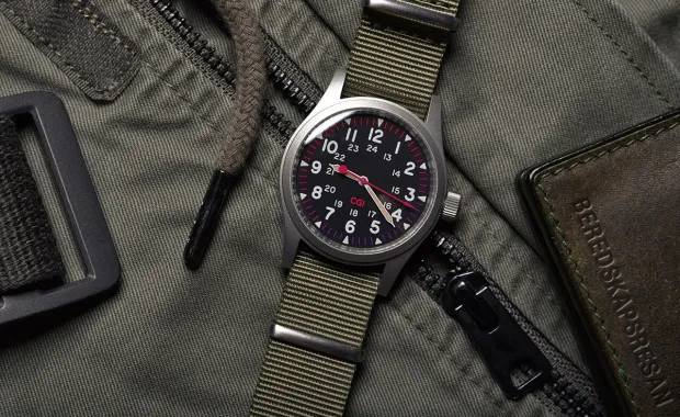 Ett armbandsur med militärgrönt klockband ligger på en militärgrön väska