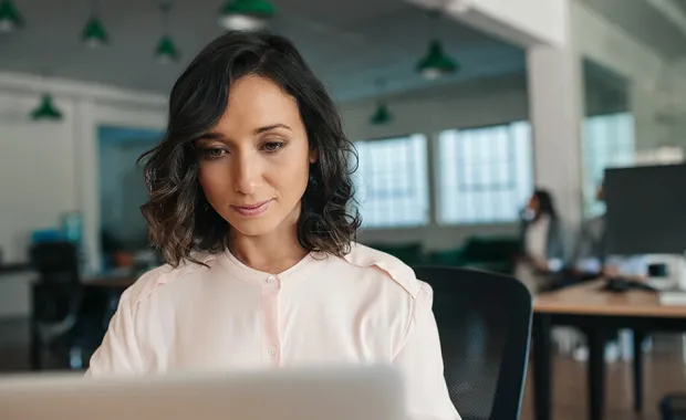 Kvinna som tittar på sin laptop i ett öppet kontorslandskap