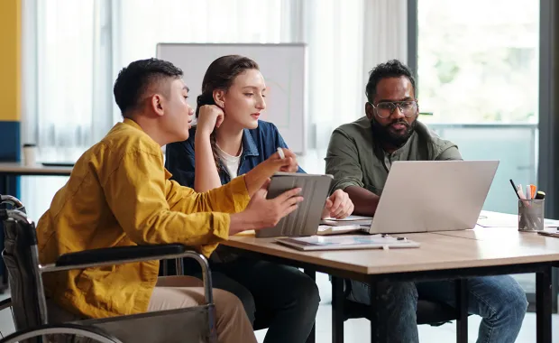 Three people working together, looking at a laptop