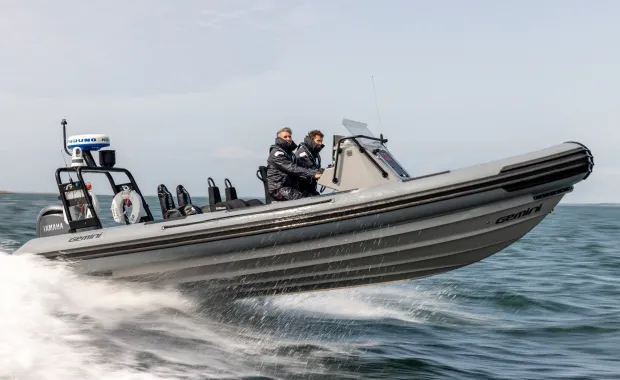 Two people ride in a rigid inflatable motorboat speeding across the water