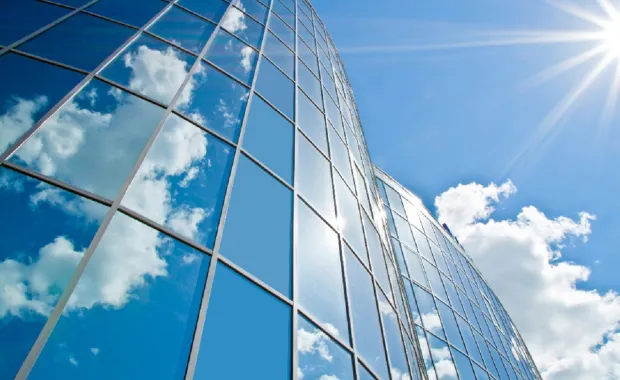 Ein Gebäude aus Glas wird von der Sonne angestahlt und reflektiert den Himmel und Wolken