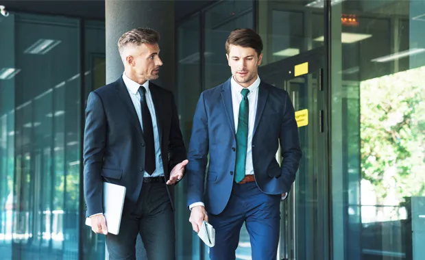 Two people in business attire have a discussion as they walk