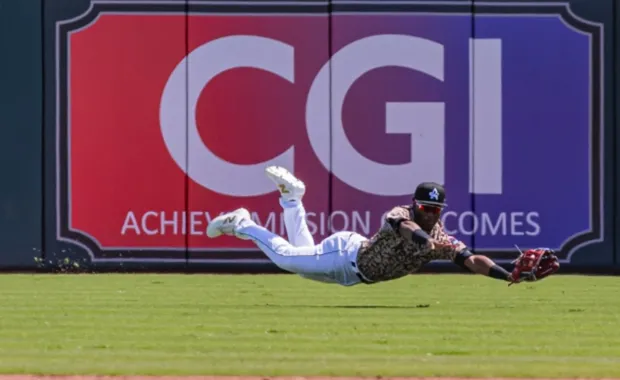 CGI logo in the outfield of the Trash Panda stadium in back of a baseball player diving for a ball
