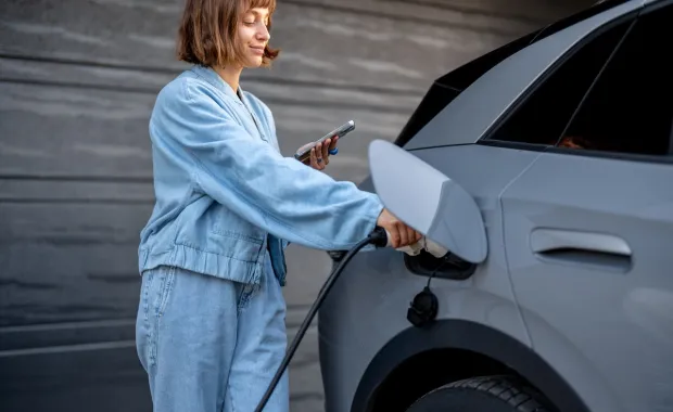 Woman checks her phone while charging an electric car