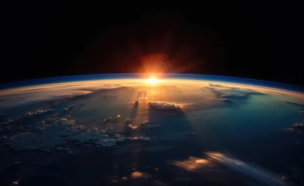 Earth’s curved horizon seen from space, with a sunrise casting light across the atmosphere