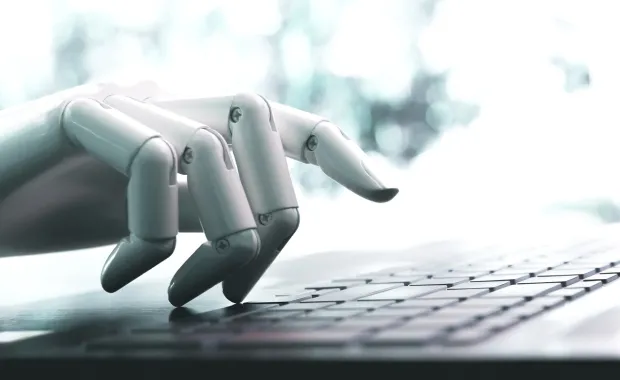 robot hand representing chatbots and intelligent automation typing on a laptop