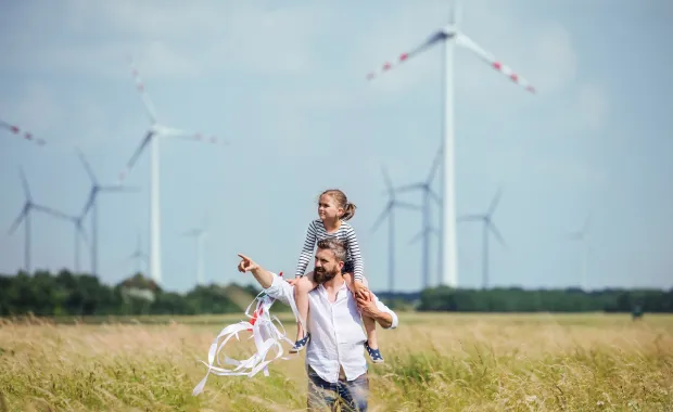 Child riding on shoulders of an adult pointing and walkthrough through a turbine field
