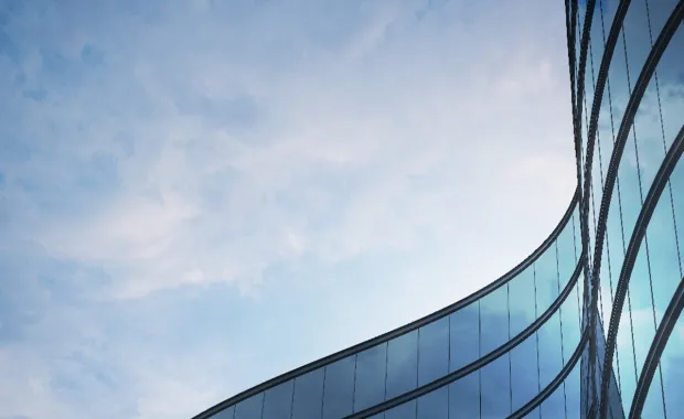 Curved glass facade of a modern building reflecting a cloudy blue sky