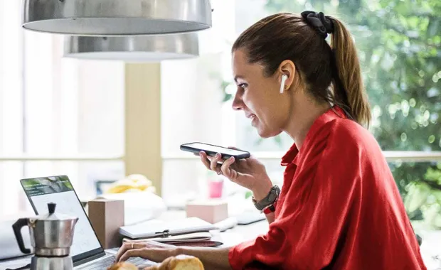 Kvinna sitter hemma vid köksbordet och arbetar framför sin laptop samtidigt som hon tittar på sin laptop