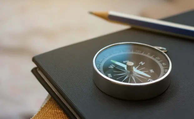 Kompass liegt auf einem Buch daneben ein Bleistift