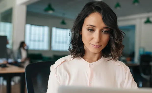 Kvinna sitter och jobbar koncentrerat vid sin laptop i ett öppet kontorslandskap
