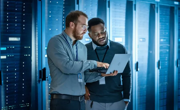 two data professionals review information on a laptop in a data center