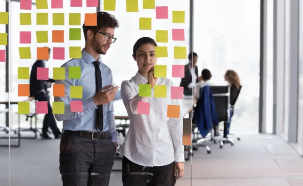 Zwei IT-Berater stehen vor einer gläsernen Wand mit Post-its