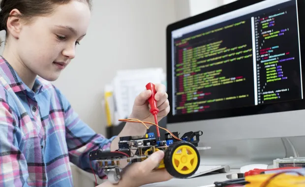 En flicka sitter framför dataskärm med kod och jobbar koncentrerat med sin robotmodell
