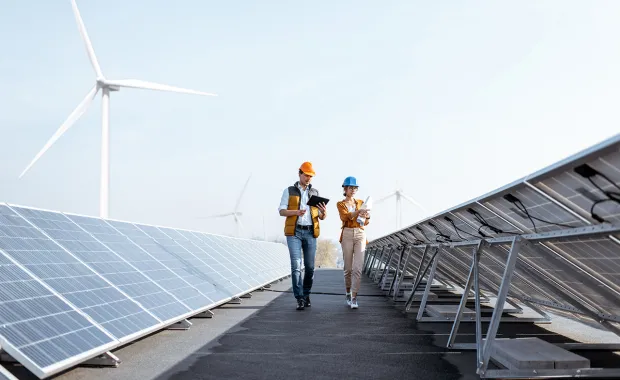 two people walking between solar panels with a wind turbine in the background