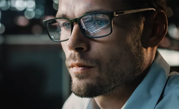 Developer with software computer screen reflected in his glasses