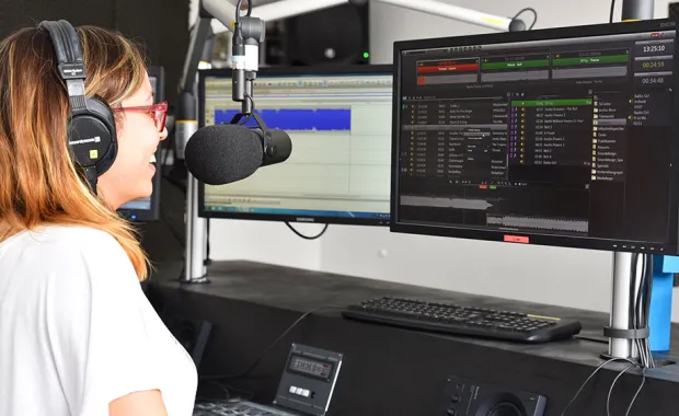 Eine Radiomitarbeiterin sitzt vor einem Bildschirm und verwendet CGI dira Onair Player