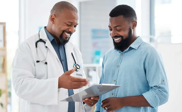 male doctor talking and smiling with patient and looking down at an ipad 