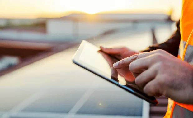 Man in high-vis jacket using a tablet on a solar farm