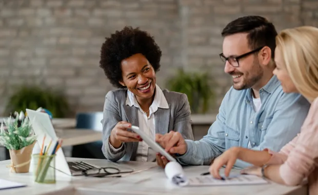 Insurance advisor and a couple reviewing information on a digital tablet at a desk