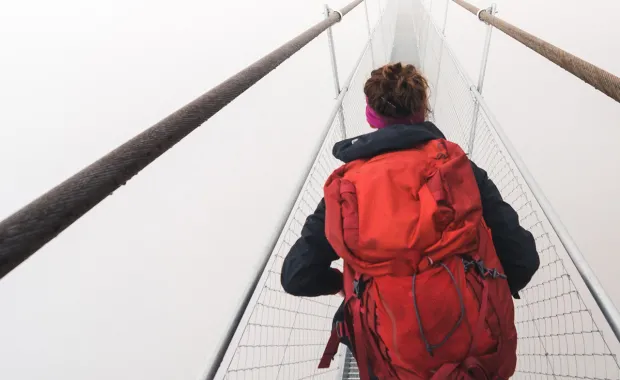 Kvinna med stor röd ryggsäck går över en hängbro i dimma
