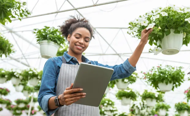 Woman tending to plants holding ipdad in a greenhouse