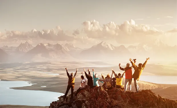 En grupp med vandrare står på ett berg och sträcker ut händerna.