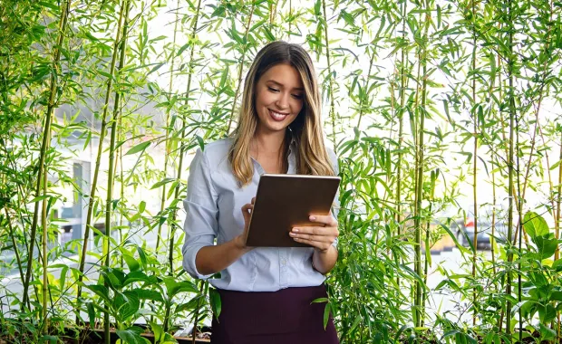 Frau mit Laptop steht vor einer grünen Pflanzenwand