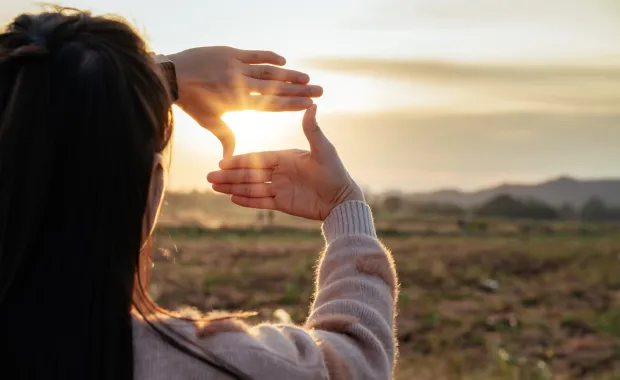 Hands framing a heart in front of the sunset