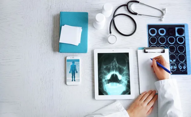 Arzt schreibt Patienteninformationen auf und nutzt dabei Iphone und Tablet