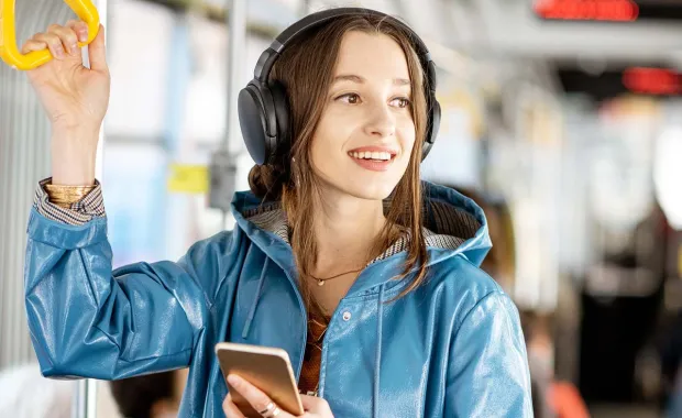 Female standing in a bus wearing headphones and looking out the window smiling