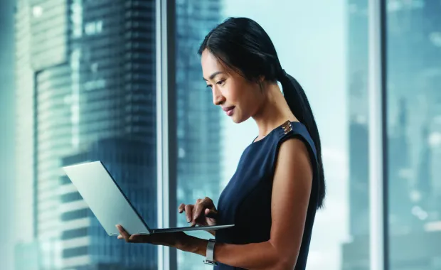 Female professional standing with laptop near office window