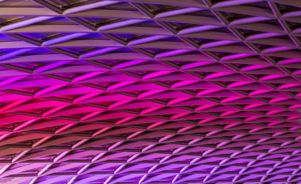 Violetin ja pinkin sävyissä valaistu geometrinen kattokuvio.