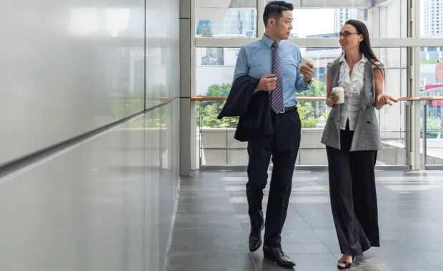 En kvinnlig och en manlig konsultkollega går och samtalar i en öppen korridor på kontoret