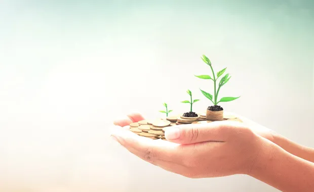 Hands holding coins with green shoots growing from them 