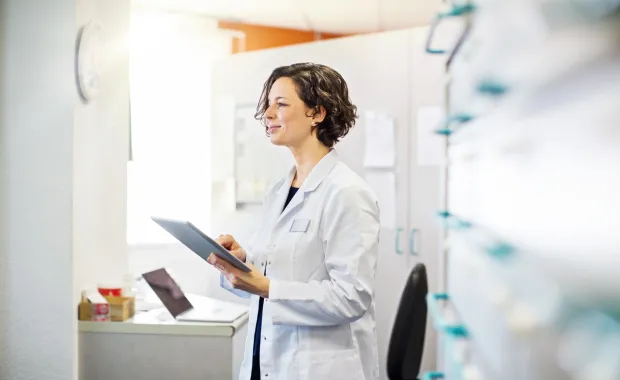 Kvinnlig läkare i vit rock står i ett rum och tittar på patientdata