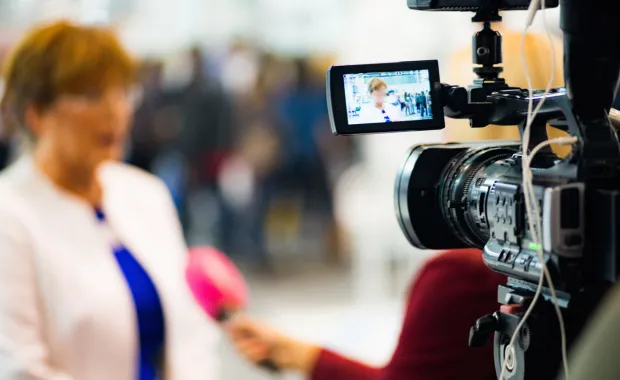 Eine Frau steht verschwommen vor einer Kamera und beantwortet Interviewfragen