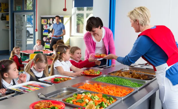 Kvinna i matbespisning på skola delar ut mat till skolelever och lärare