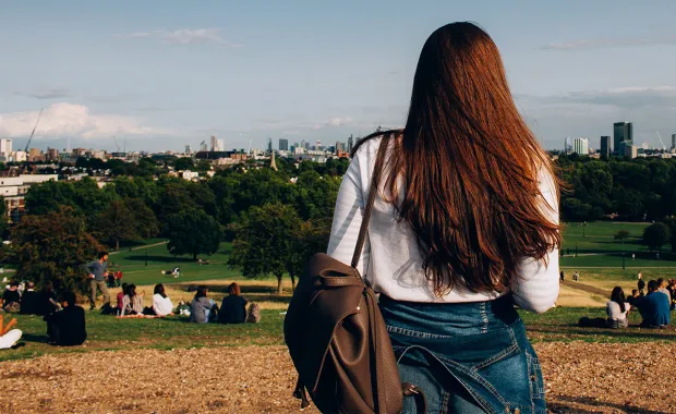 Woman standing in a park, facing London skyline 