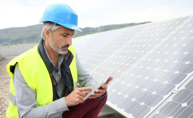 Energy engineer wearing an helmet works on his tablet next to solar panels