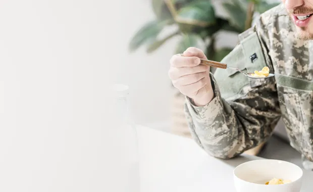 Militärklädd man sitter vid ett vitt matsalsbord och äter mat