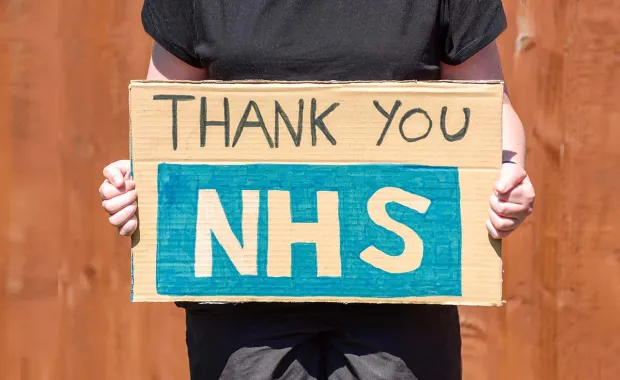 person holding up a hand made sign that says thank you NHS