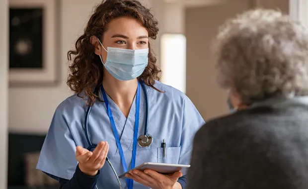 Kvinnlig läkare med munskydd samtalar med en äldre kvinnlig patient