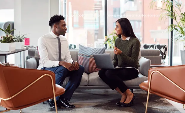 Manlig och kvinnlig kollega sitter och samtalar vid en laptop i en lounge på kontoret